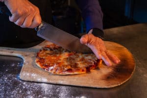 chef, using a large knife to slice a thin stonebaked pizza on a rustic wooden board at a Bainbridge Island Restaurants