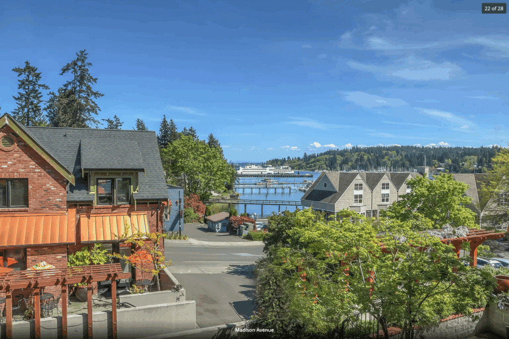 On the left, the exterior of the Eagle Harbor Inn with Eagle Harbor and the Washington State Ferry in the background. Stay at the best Bainbridge Island Lodging.
